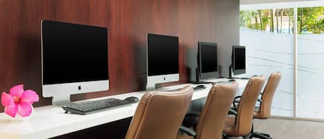 A modern office with three Apple iMacs on a white desk, leather office chairs, and a large window with a view of greenery.