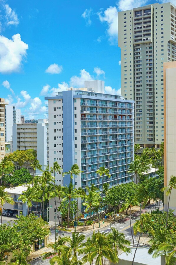 A high-rise hotel with multiple floors, surrounded by palm trees and other buildings.