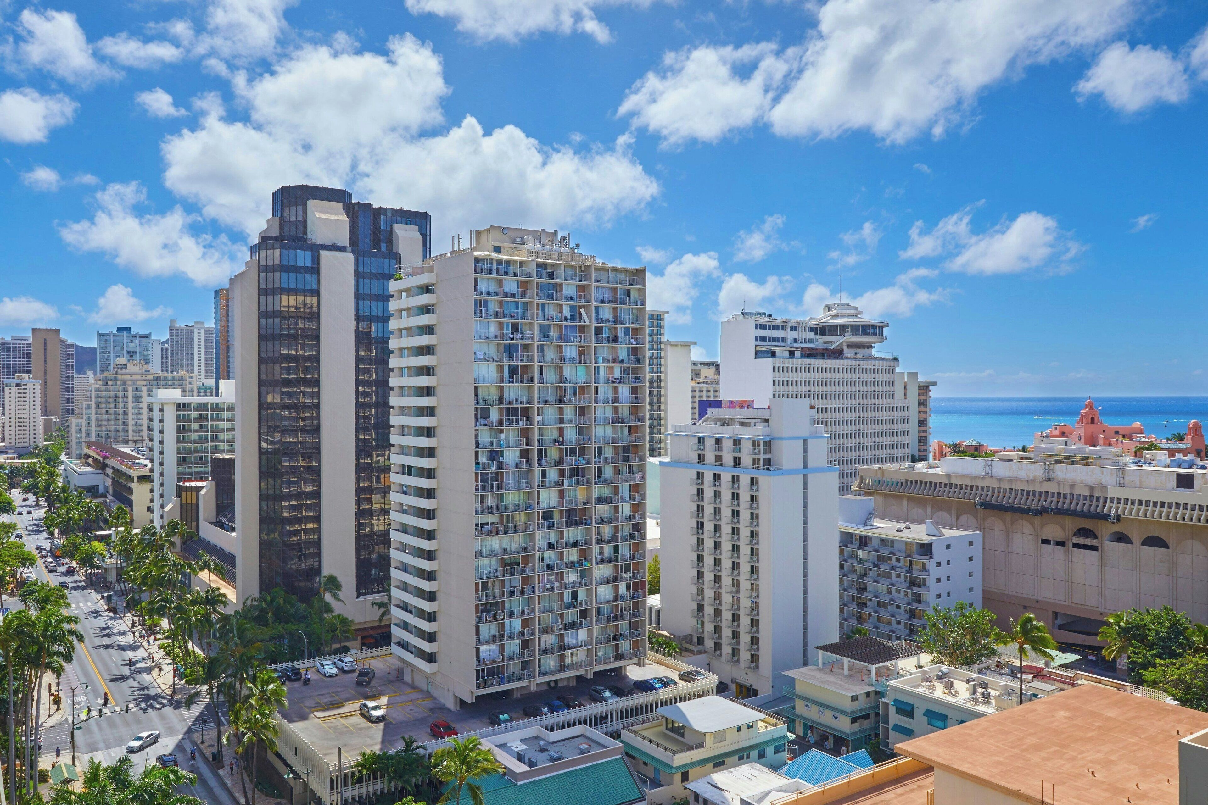 A high-rise hotel with multiple floors, a rooftop pool, and a view of the ocean.