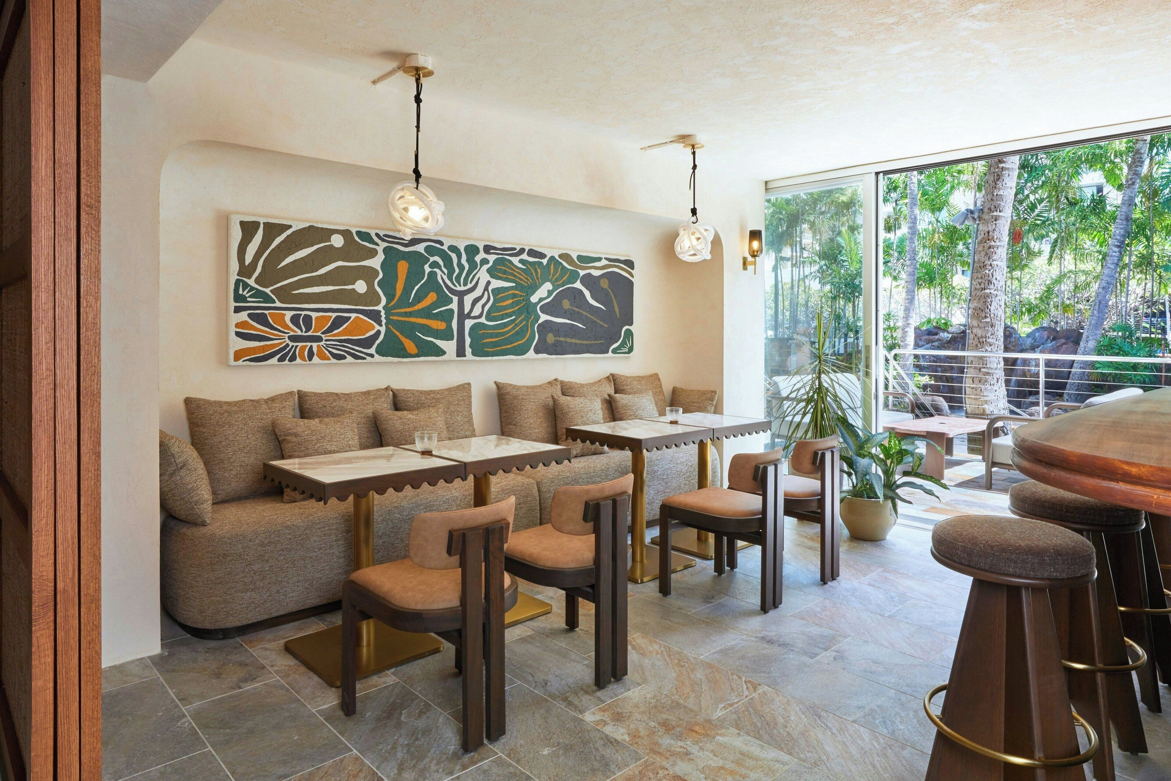 Un intérieur moderne avec un canapé, des tables et des chaises, une grande peinture abstraite au mur et une vue sur la verdure à l’extérieur.