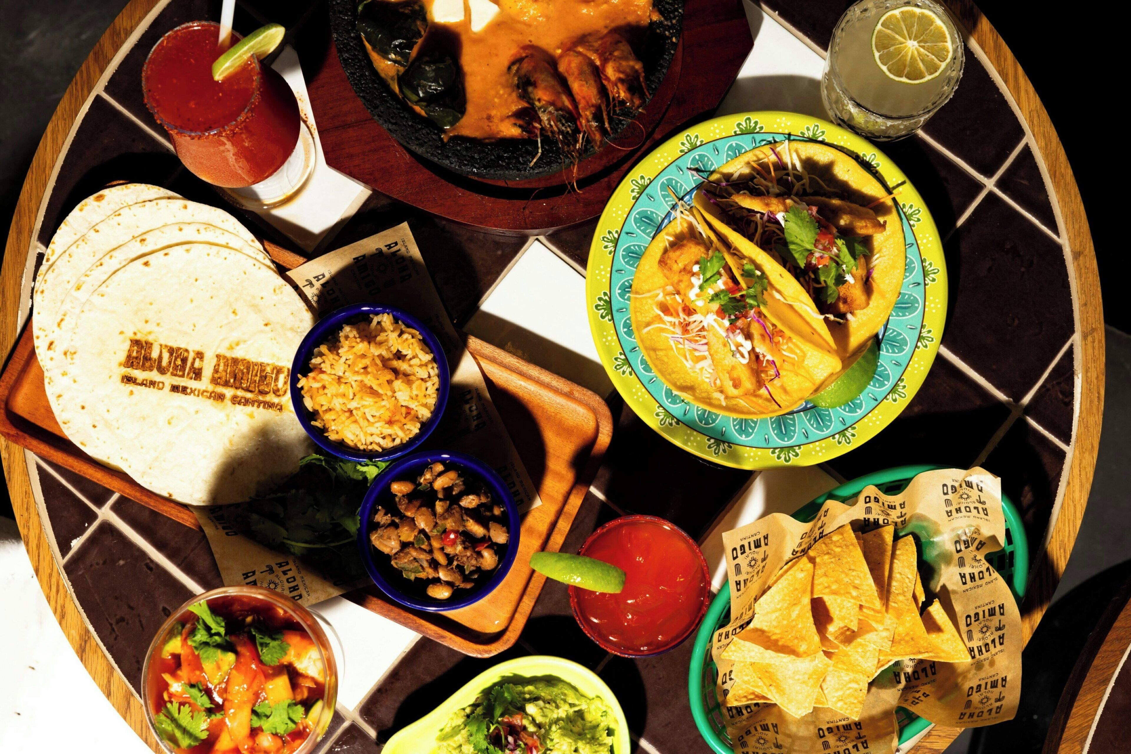 A variety of Mexican dishes including tacos, guacamole, and a margarita on a wooden tray.