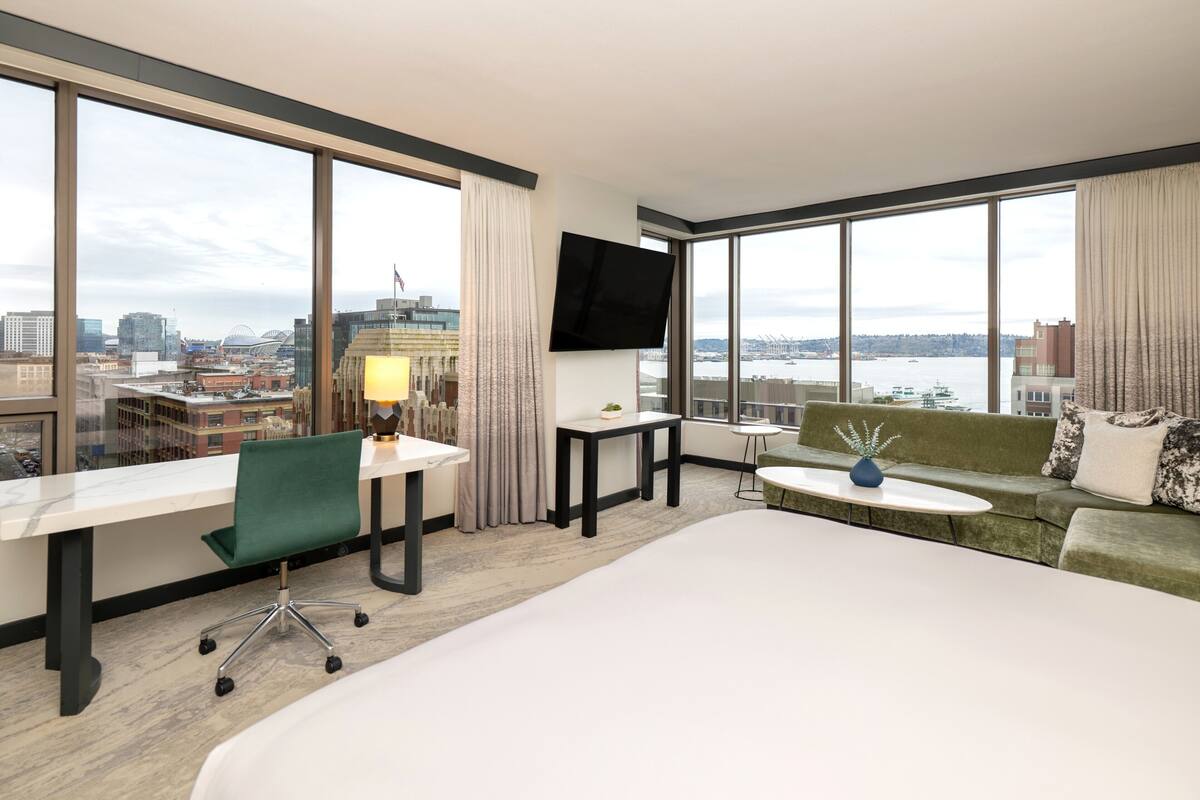 A hotel room with a large bed, a desk, a green chair, a sofa, a small table, and a TV.