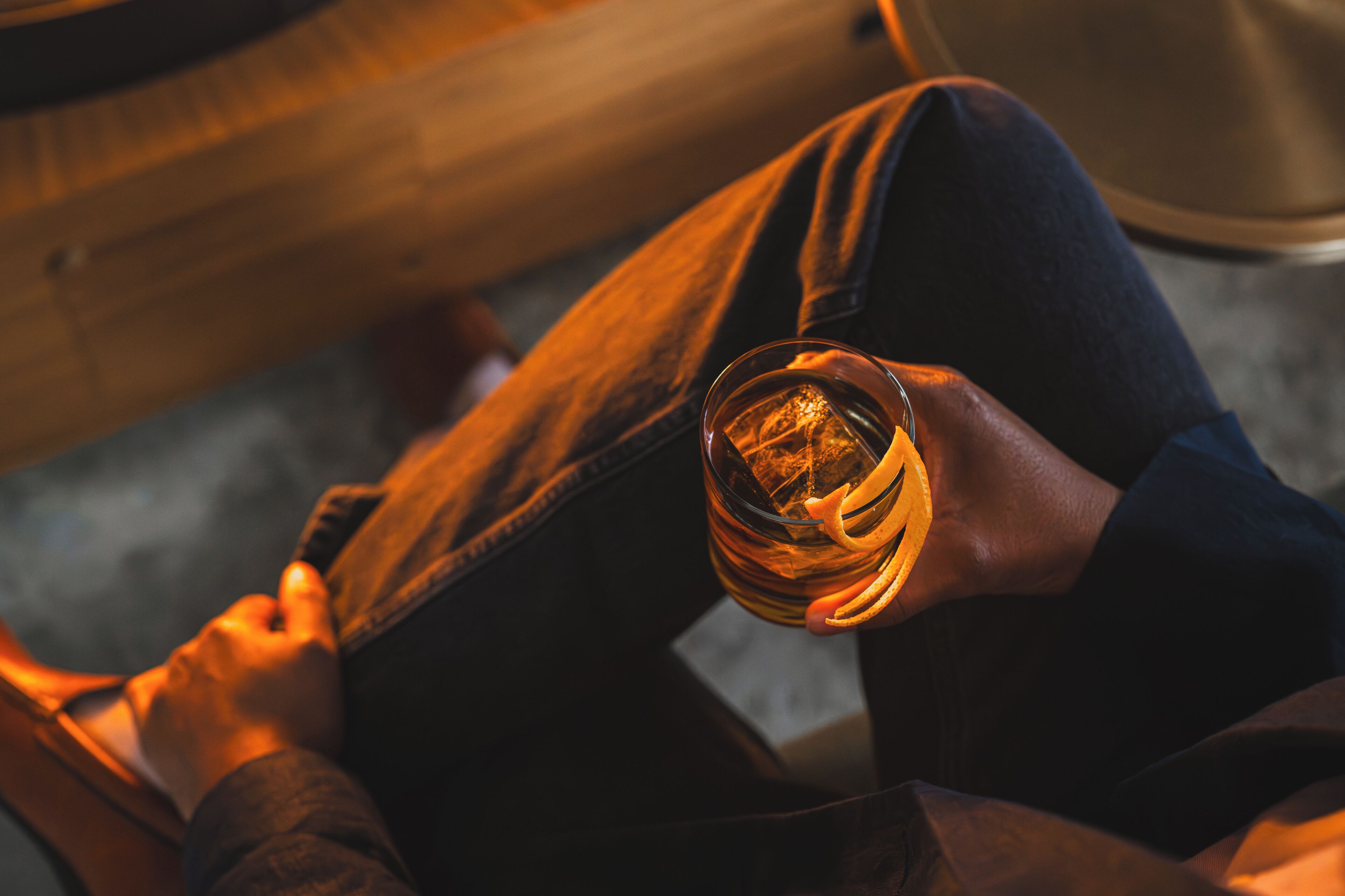 Uma pessoa sentada com um copo de uísque sobre uma superfície de madeira.