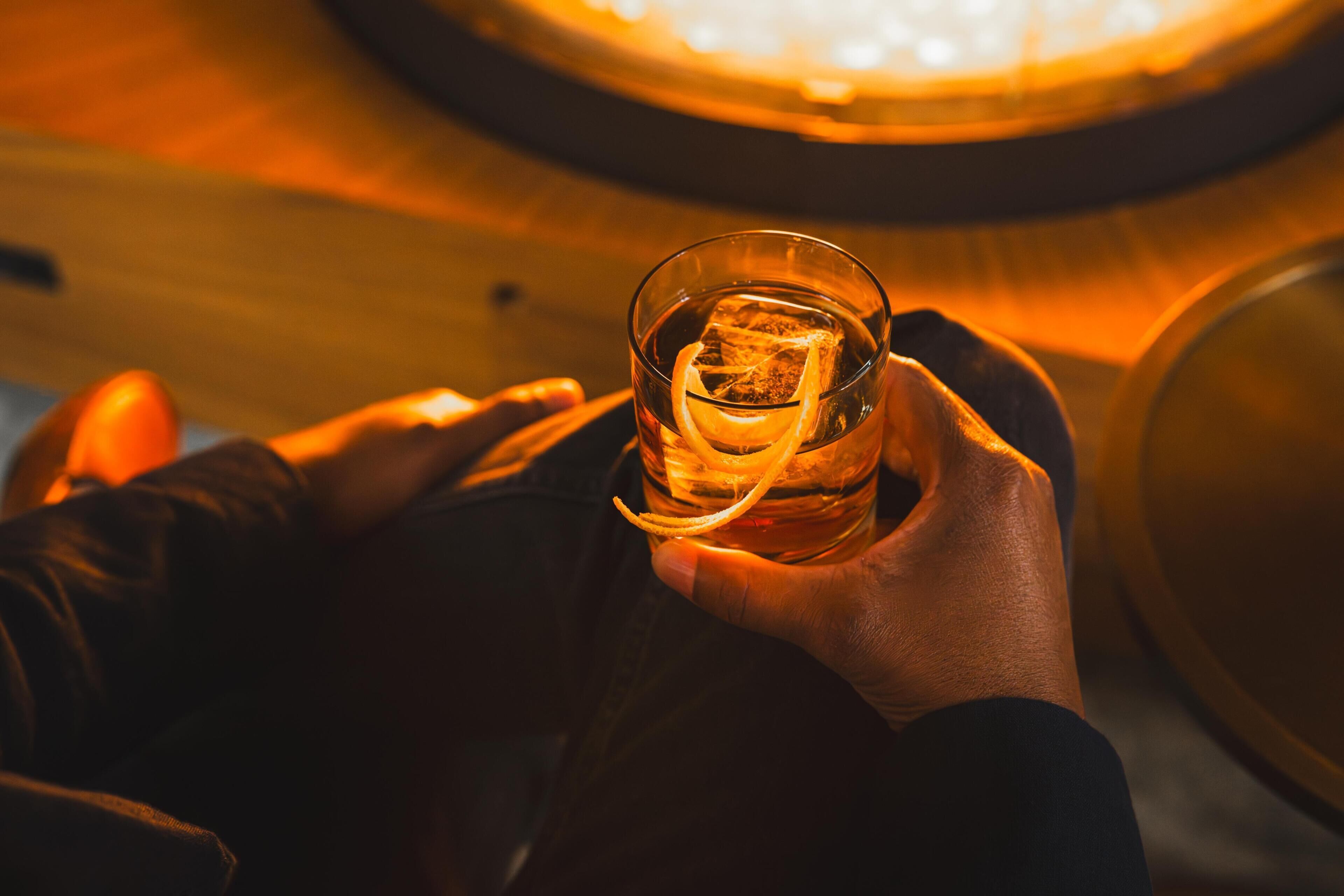 A hand holding a glass with ice cubes and a lemon slice.