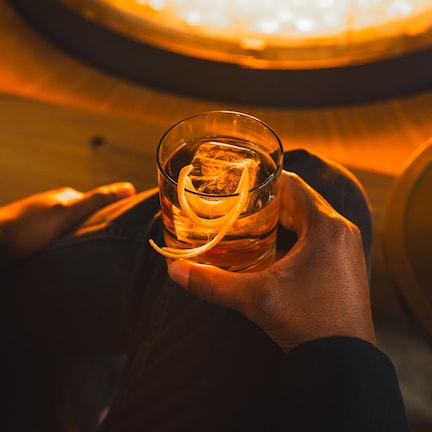 A hand holding a glass with ice cubes and a lemon slice.
