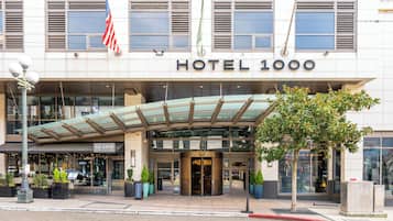A hotel entrance with a glass canopy, an American flag, and a sign reading 'HOTEL 1000'.