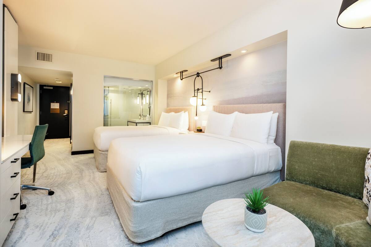 A hotel room with two beds, a sofa, a desk, and a round coffee table with a plant.