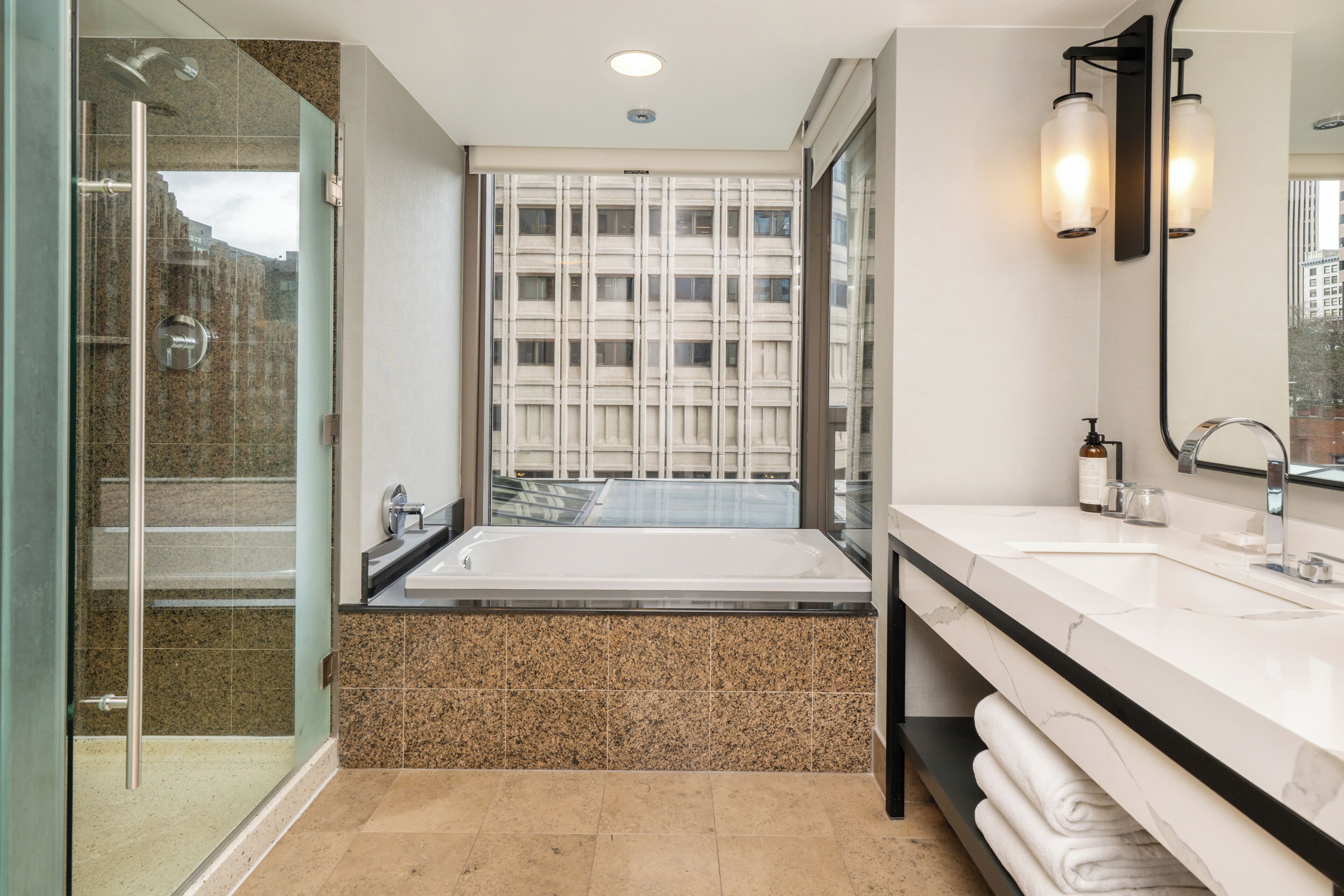 A modern bathroom with a glass shower enclosure, a freestanding bathtub, and a large mirror with wall-mounted lights.