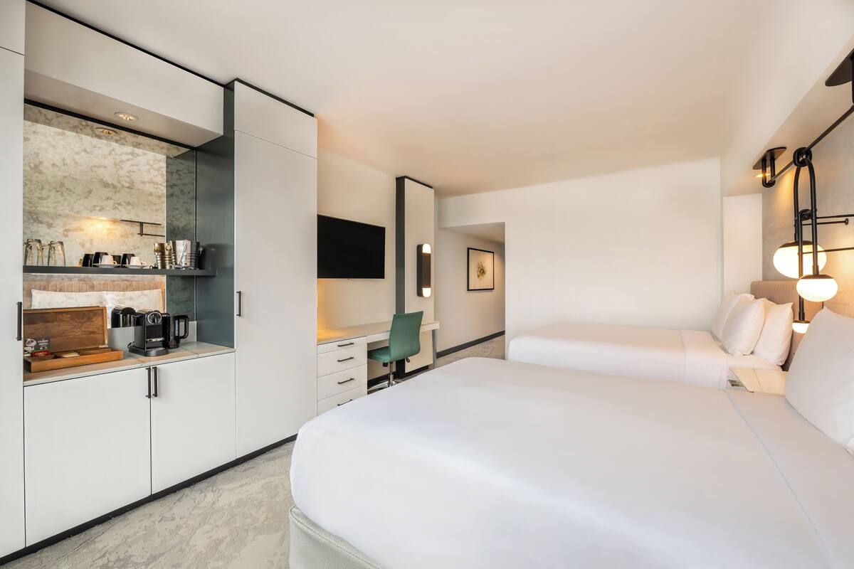 A modern hotel room with a bed, a desk, a chair, a coffee maker, and a TV.