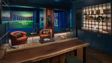 A room with a large window, a wooden bar, a sofa, and a bookshelf.