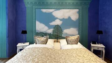 Een slaapkamer met een groot bed, twee nachtkastjes en een muurschildering van een boom en lucht.