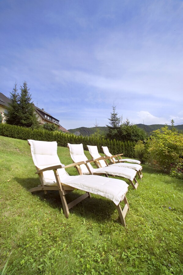 Cuatro sillones de madera con cojines blancos en un área verde al aire libre.
