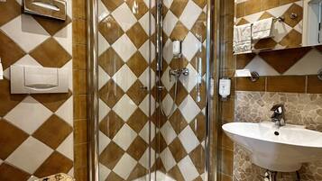 A bathroom with a glass-enclosed shower, a toilet with a mosaic seat, and a sink with a stone-patterned backsplash.