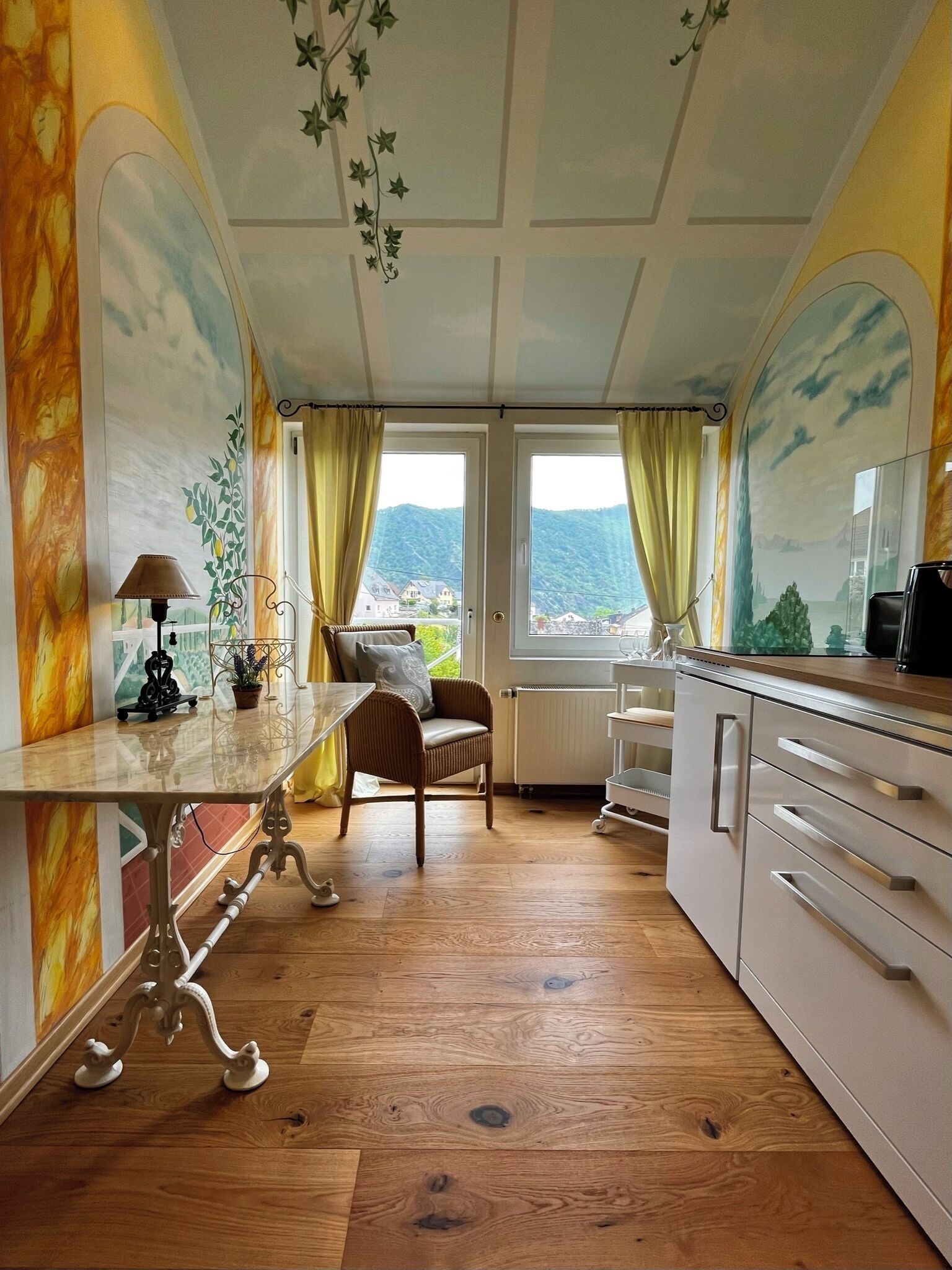 Une pièce comprenant une table à manger, une chaise, un canapé, un coin cuisine et donnant sur l’extérieur.