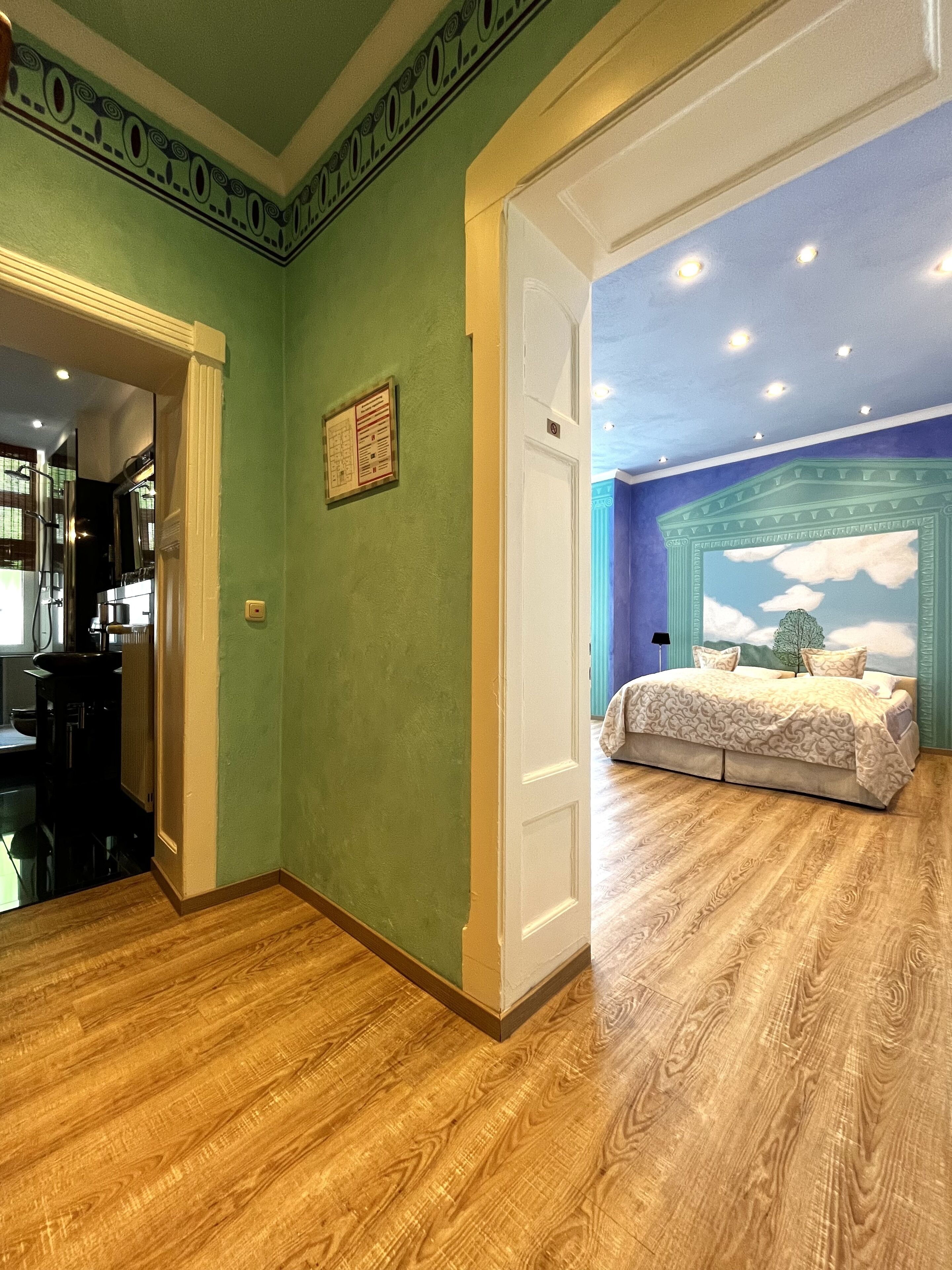 A room with a bed, a blue ceiling mural, and a green wall.