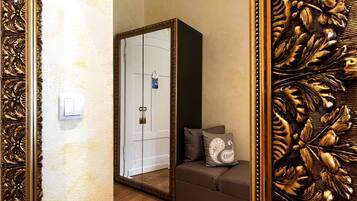 Een kamer met een houten vloer, een bank met kussens, een deur en een spiegel met decoratief gouden omlijsting.