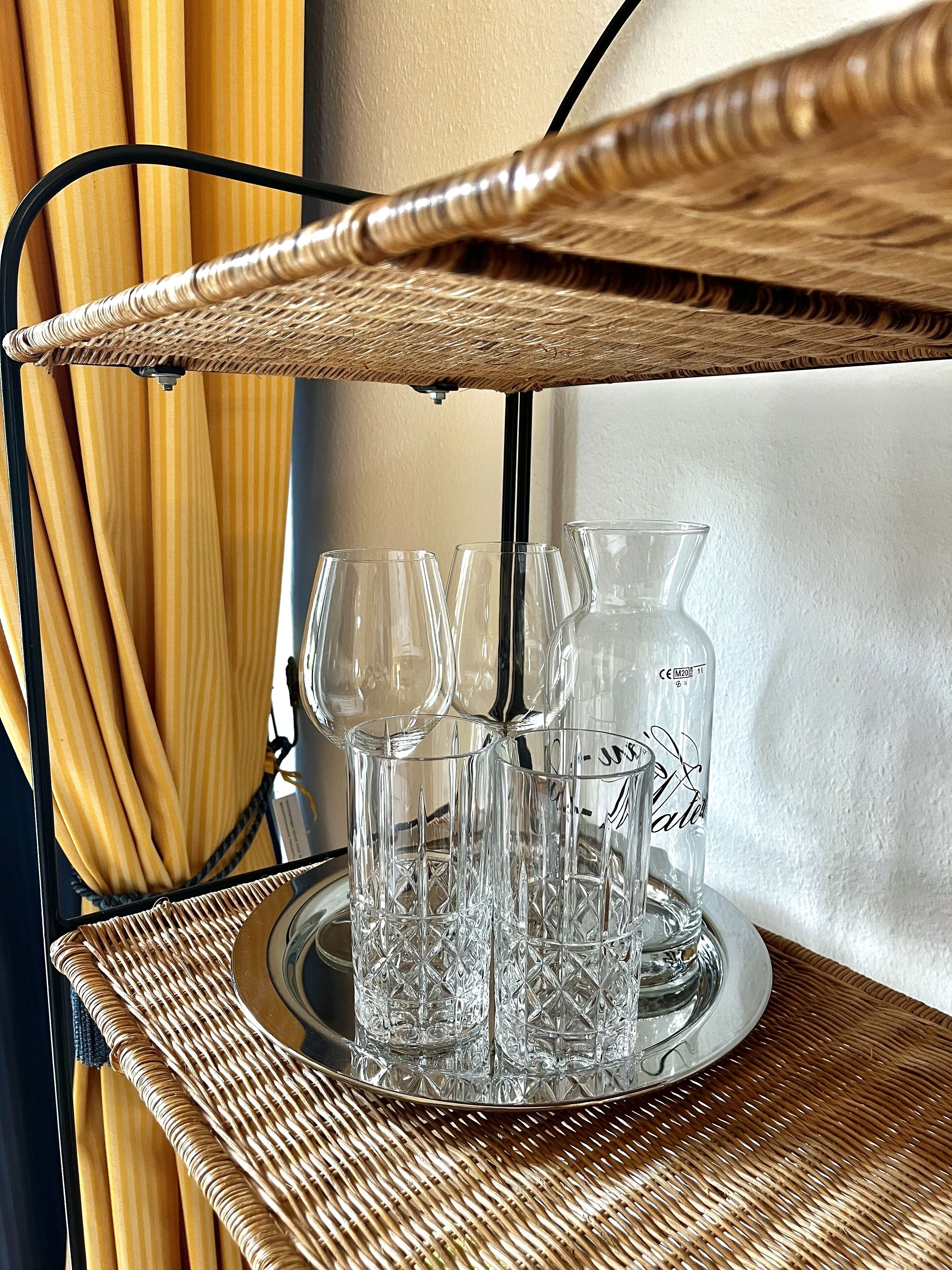 A wicker table with a glass tray holding wine glasses and a bottle.