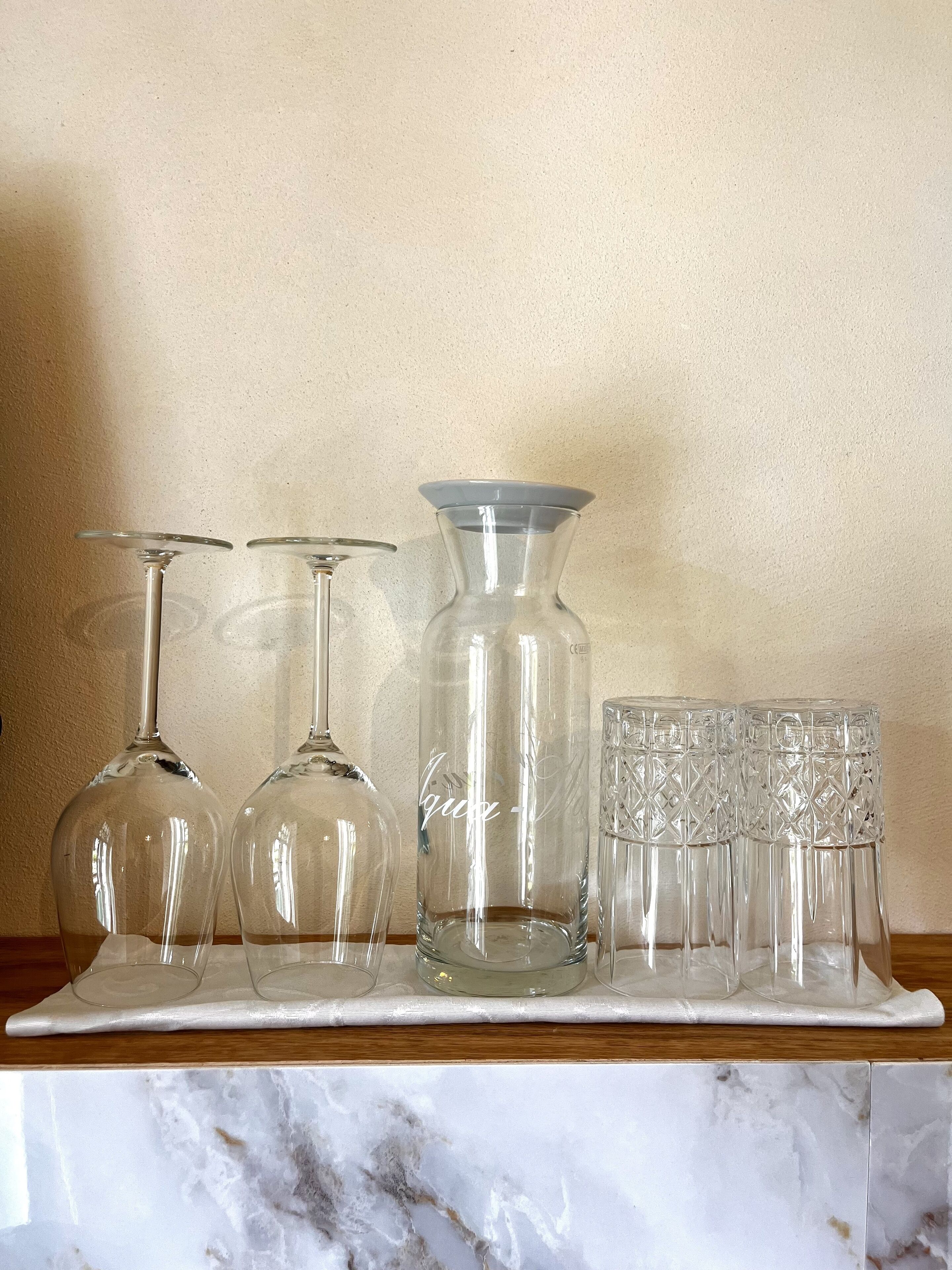 A marble-tiled countertop with a glassware set including wine glasses, a decanter, and a set of glasses.