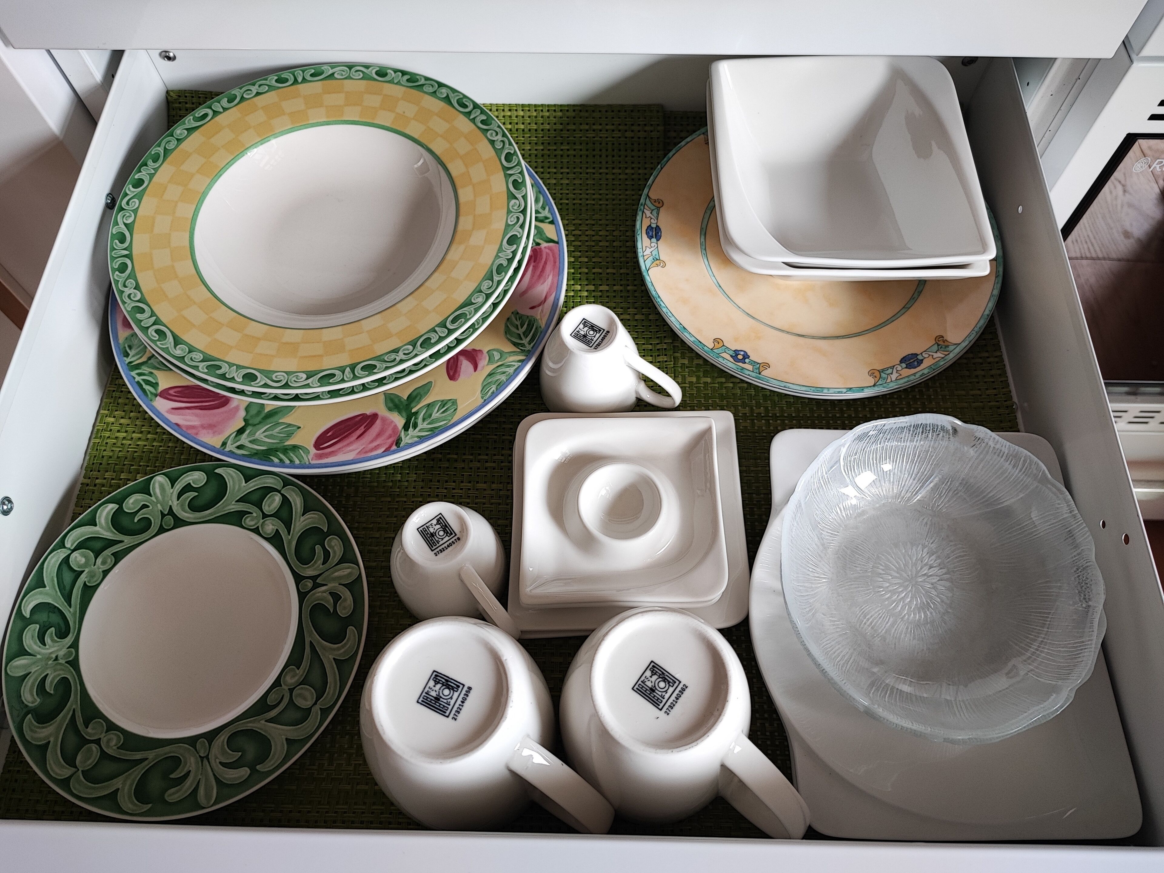 A drawer containing various white ceramic dishes, including plates, bowls, and cups, with decorative patterns.