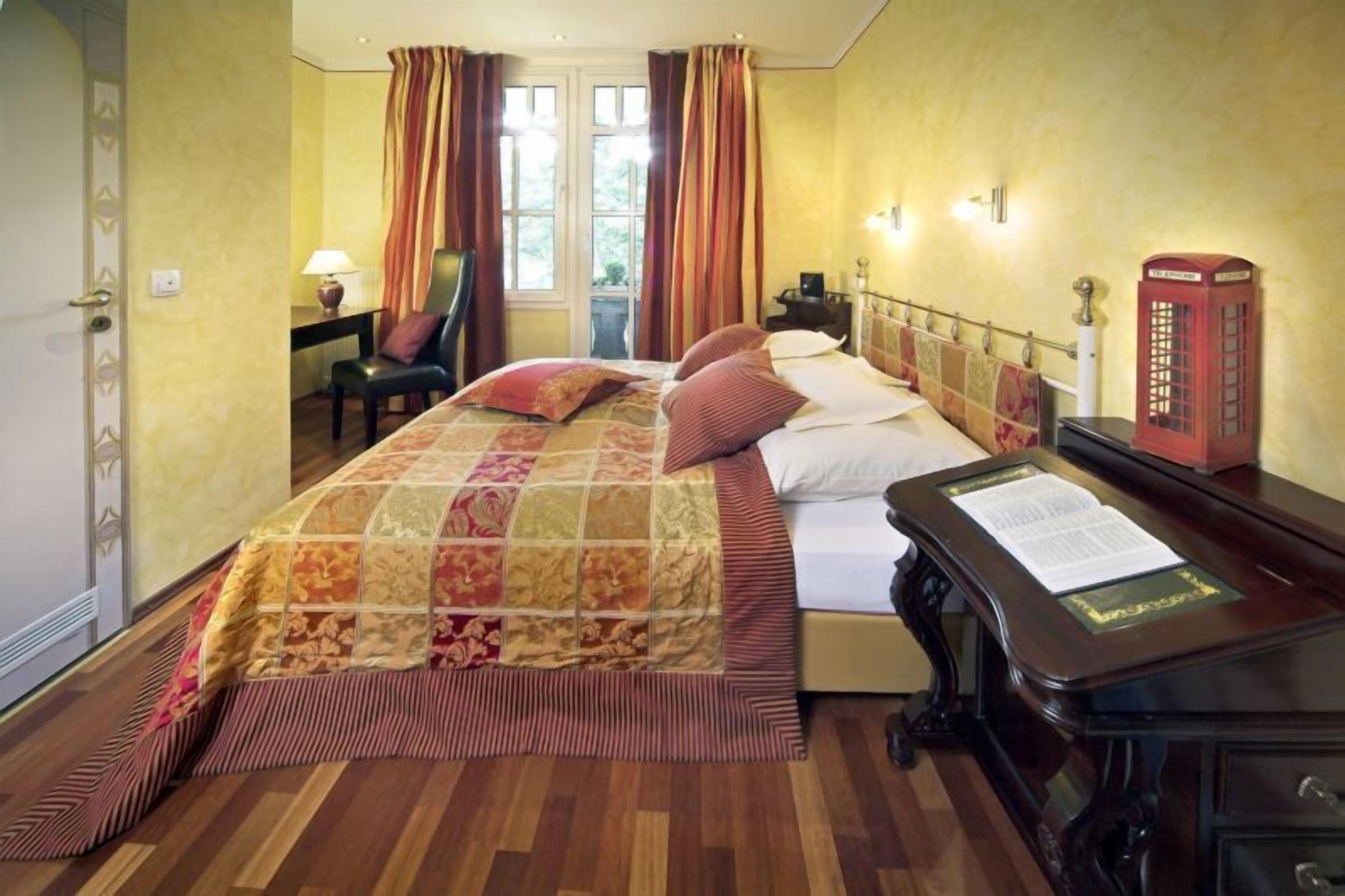Quarto de hotel com uma cama, uma mesa com telefone e uma janela com cortinas.