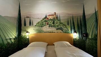 A room with a mural of a castle on the wall, a bed with white linens, and two bedside lamps.