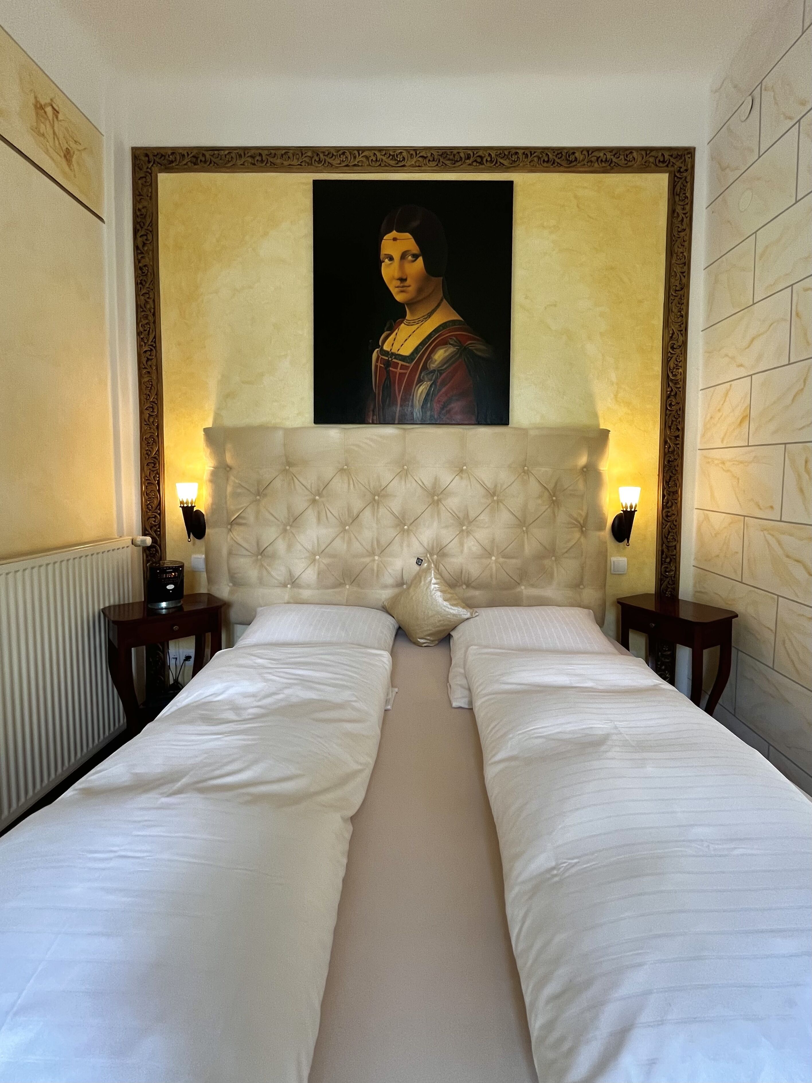 Une chambre d’hôtel avec un grand lit, deux tables de chevet, une tête de lit décorative et un tableau encadré au mur.