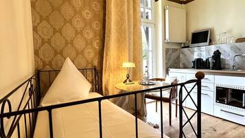 A bedroom with a metal bed frame, a bedside table with a lamp, and a view of the kitchen area.