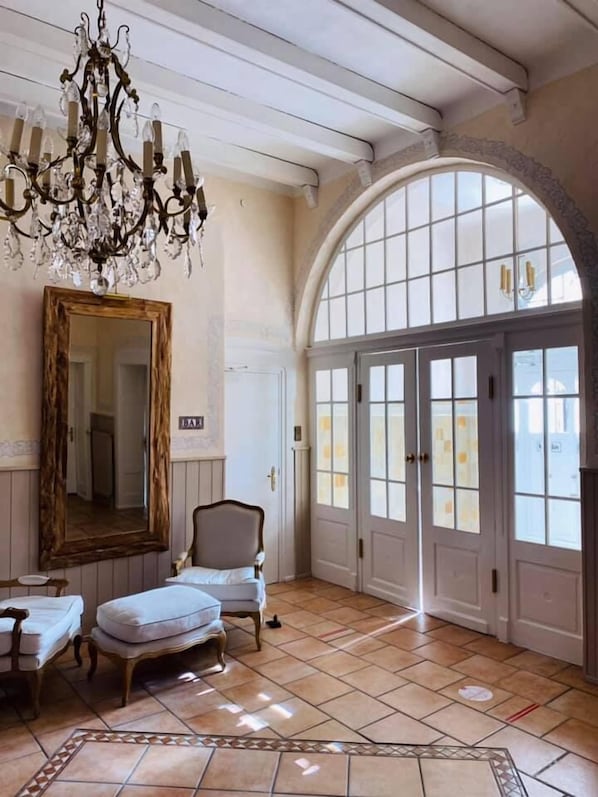 A room with a large mirror, a chandelier, a chair, and a large arched window.