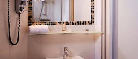 A bathroom with a hairdryer, a towel rack, a glass shelf with toiletries, and a sink.