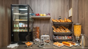 Um buffet de café da manhã com diversos alimentos, geladeira e um espaço para café.