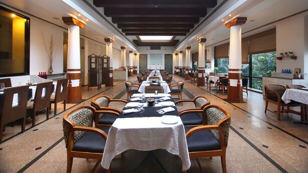 Uma ampla sala de jantar com longas mesas, cadeiras e teto alto com vigas de madeira.