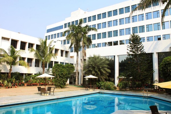 A modern hotel with a swimming pool, palm trees, and a clear blue sky. - Hotel Maurya (Patna)