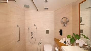Un baño moderno con ducha, inodoro y lavamanos, que incluye un espejo, toallero y una planta pequeña.