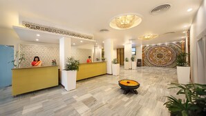 Uma área de recepção de hotel com design moderno, incluindo um balcão de atendimento, painéis decorativos na parede e um carpete estampado.