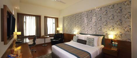 A hotel room with a large bed, a desk with a chair, a TV, and a ceiling fan.