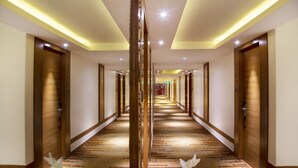 Corredor de hotel com portas de madeira, carpete estampado e luminária central.