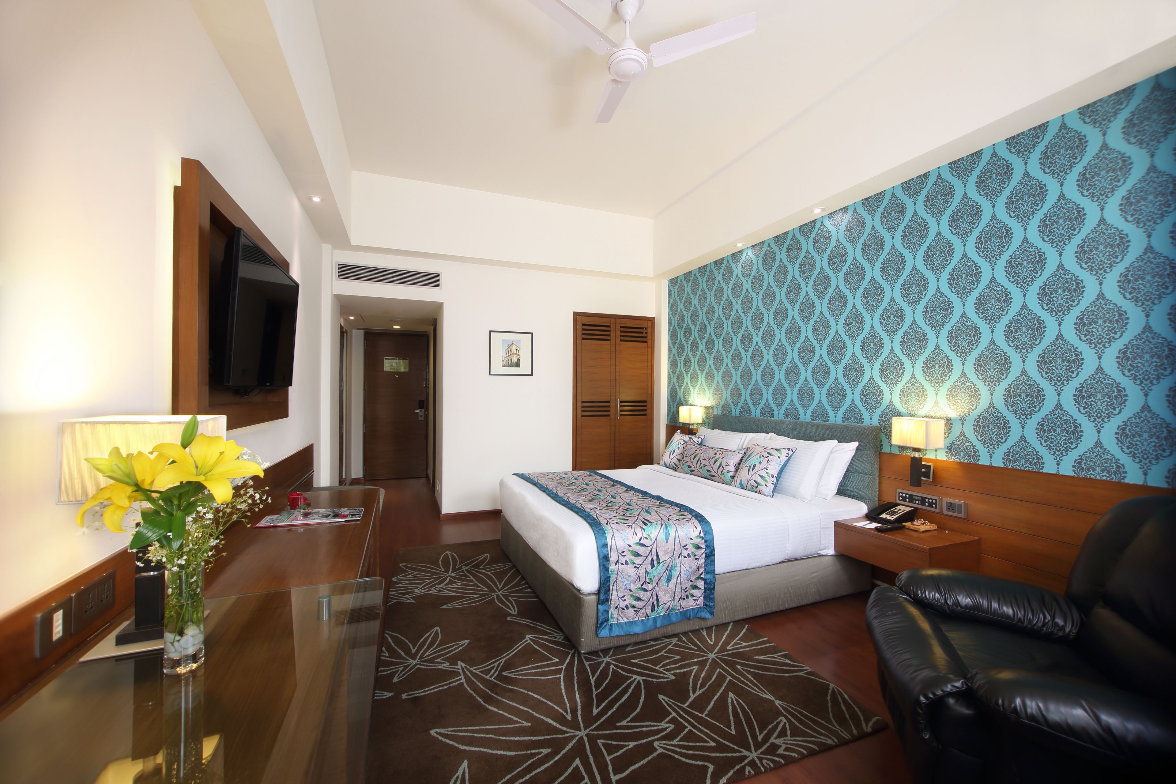 Habitación de hotel con cama, escritorio, silla, televisor y pared con diseño.