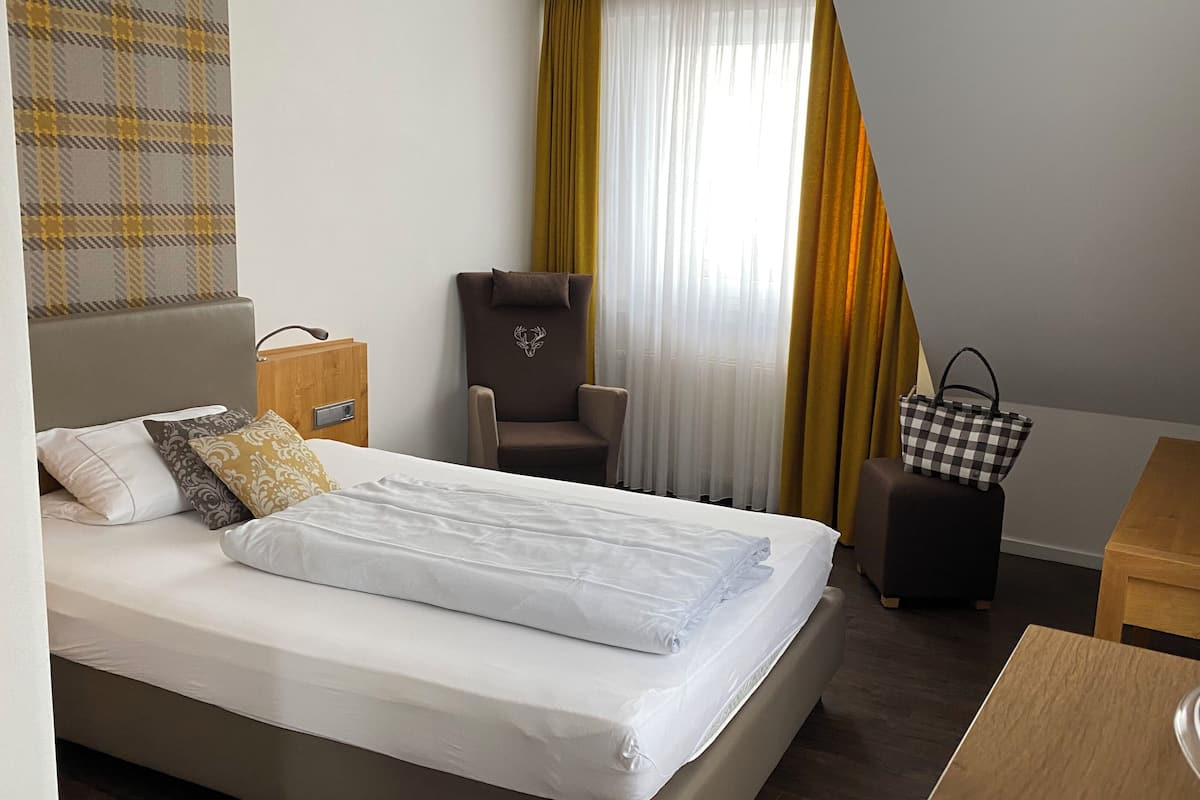 Ein Hotelzimmer mit Bett, Stuhl, Schreibtisch, Koffer und Handtasche.
