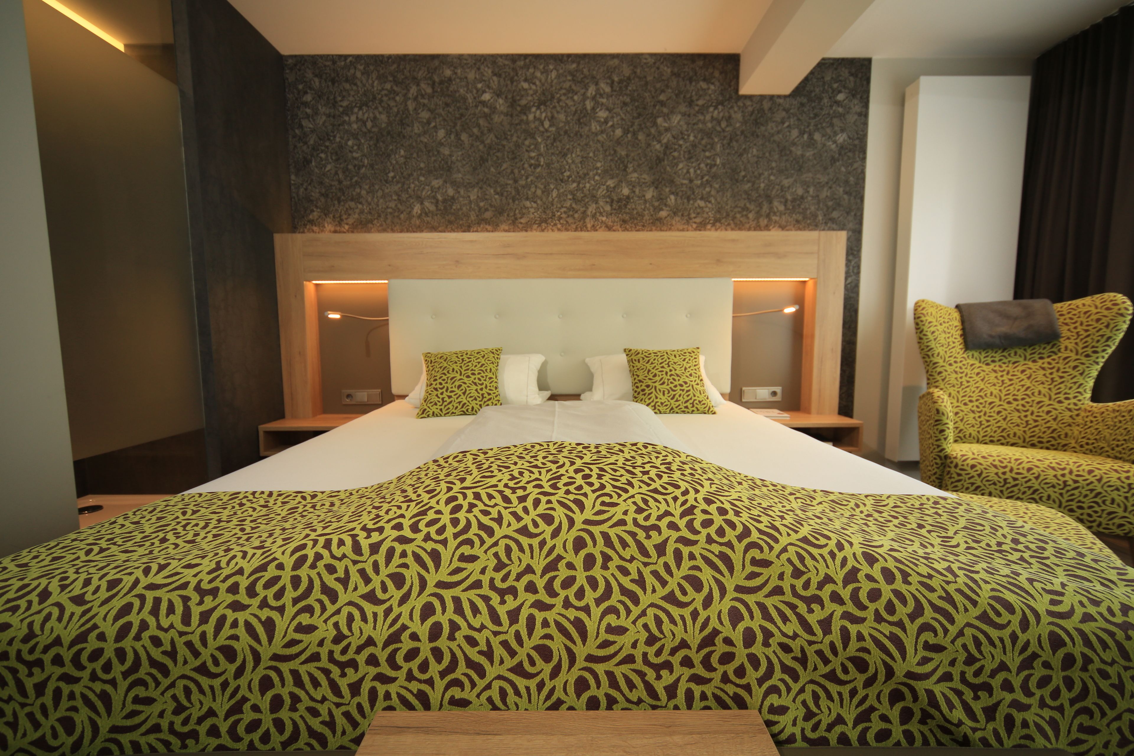 Una habitación de hotel con una cama grande, un cabecero de madera, dos mesitas de noche con lámparas y una colcha estampada.