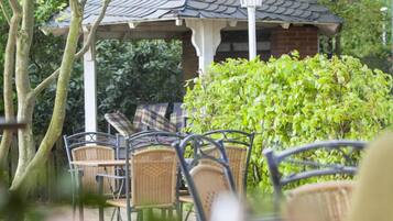 A gazebo with a tiled roof, surrounded by lush greenery and wicker furniture.