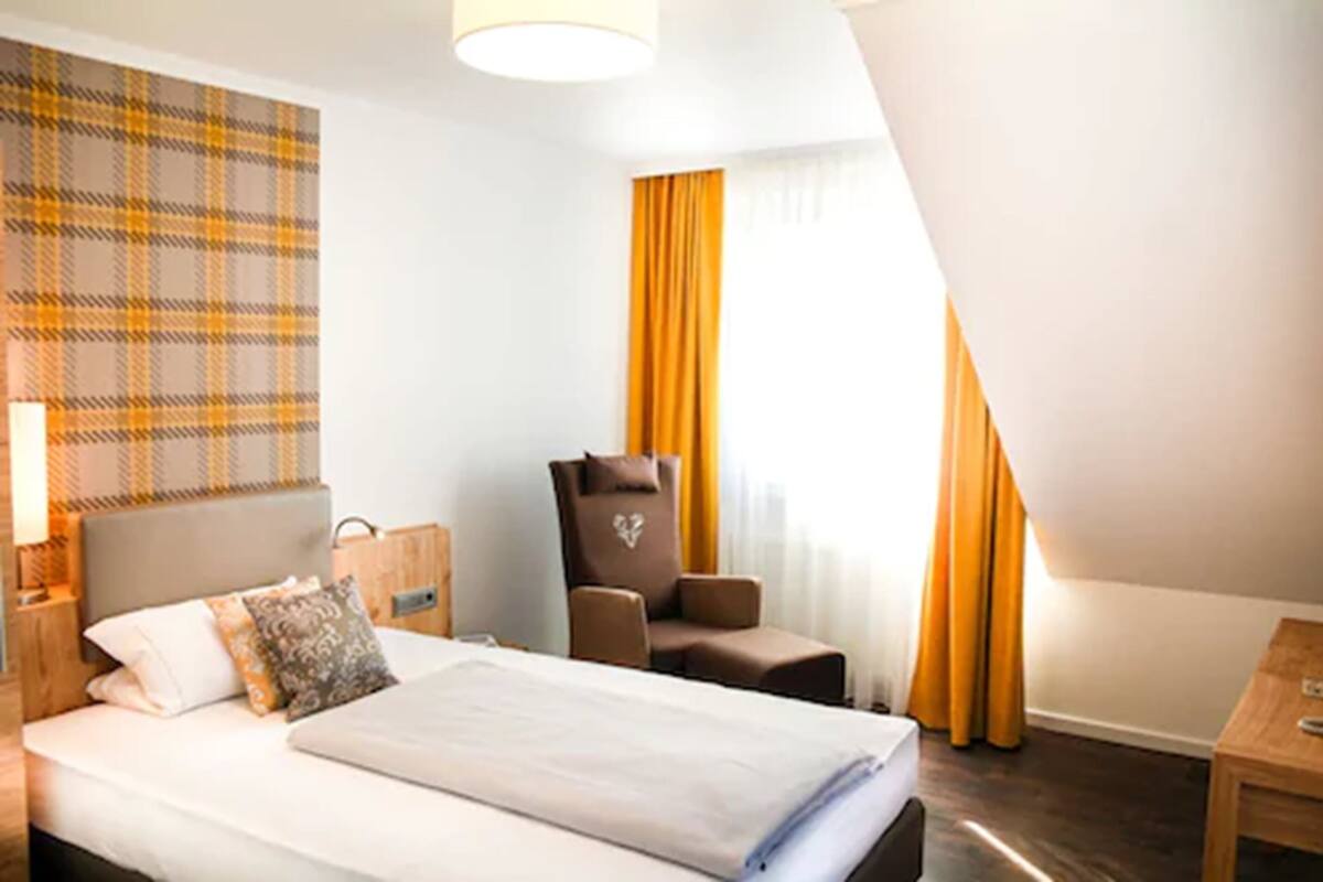 Ein Hotelzimmer mit Bett, Stuhl, Schreibtisch und einem fenster mit Vorhängen.