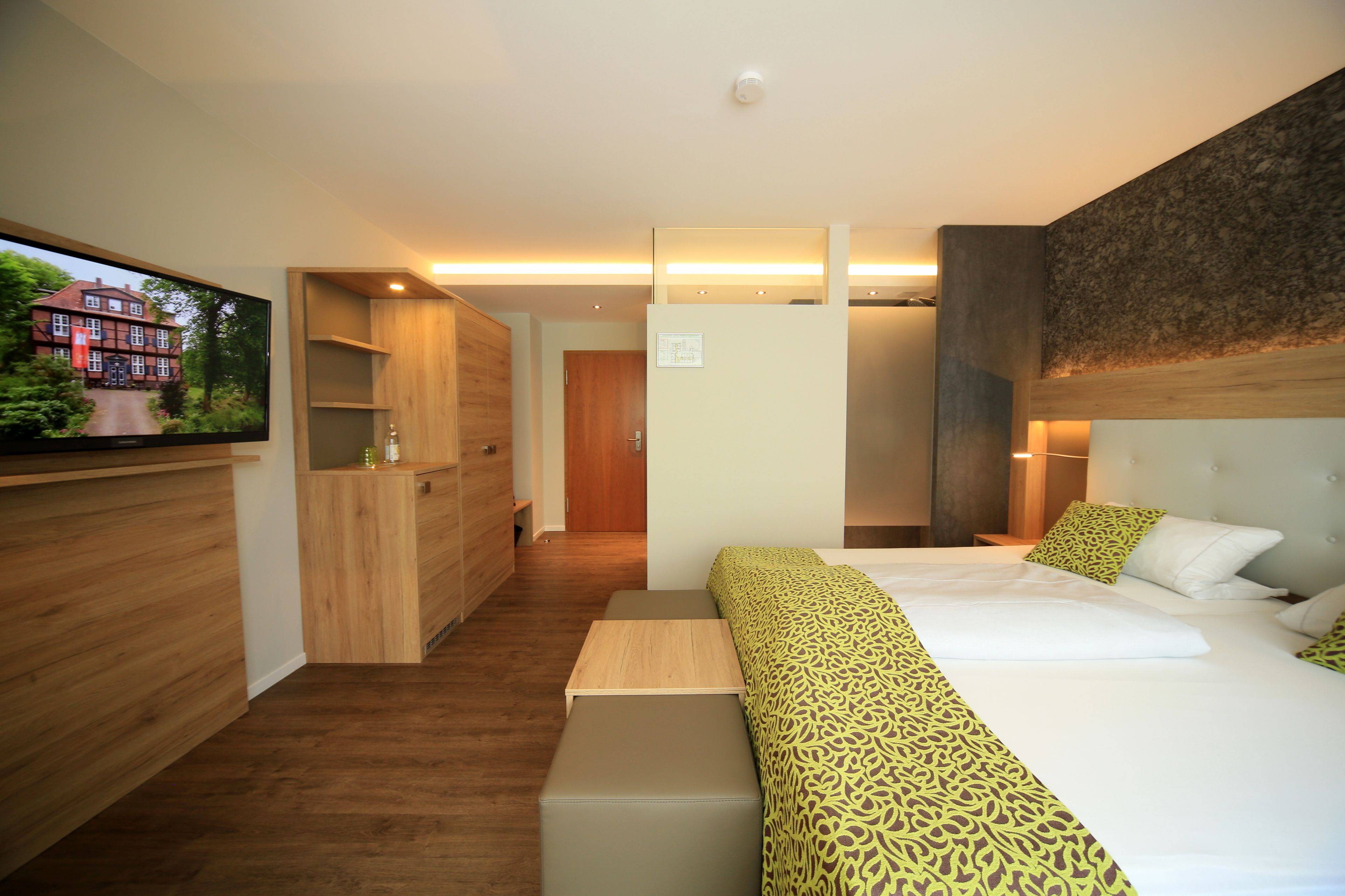 A modern hotel room with a large bed, a wooden bench, a TV, and a wardrobe.