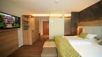 A modern hotel room with a large bed, a wooden bench, a TV, and a wardrobe.