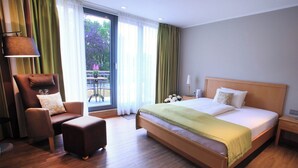 Une chambre d’hôtel avec un grand lit, une chaise, une petite table et une vue sur la verdure.
