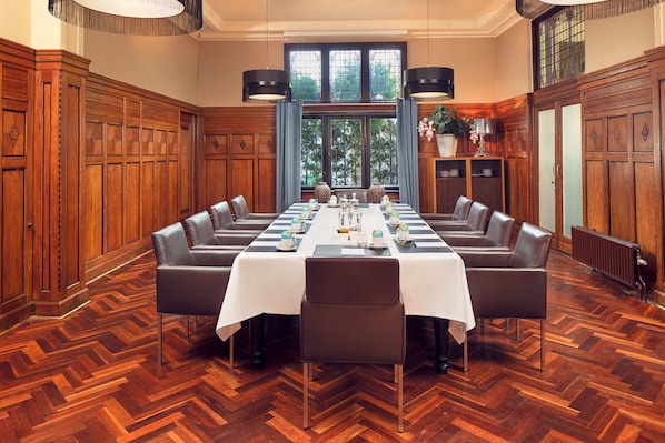 A formal dining room with a long table set for a meal, flanked by wooden paneling and large windows.