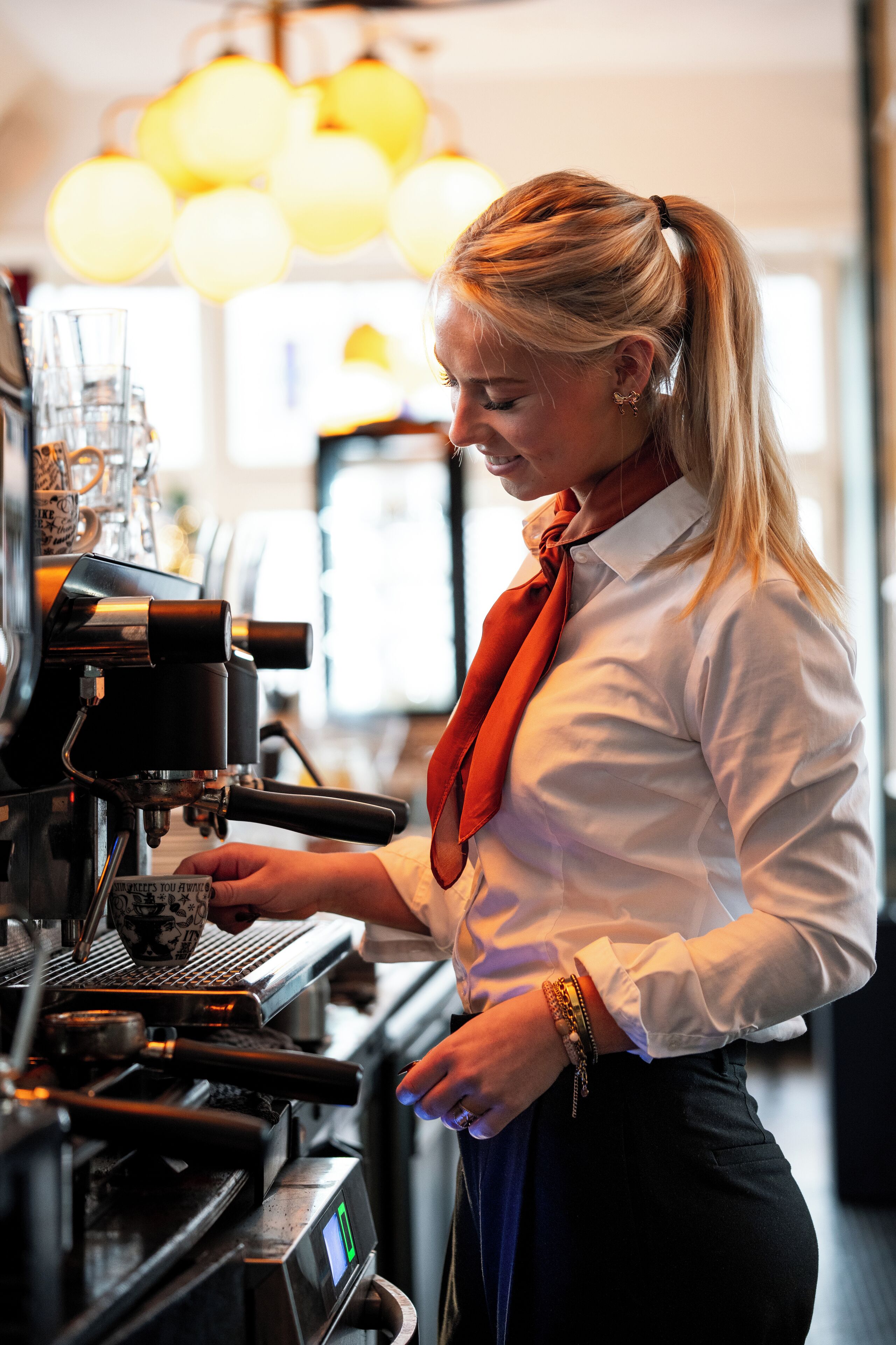 Un barista frente a una máquina de café en un espacio interior bien iluminado.