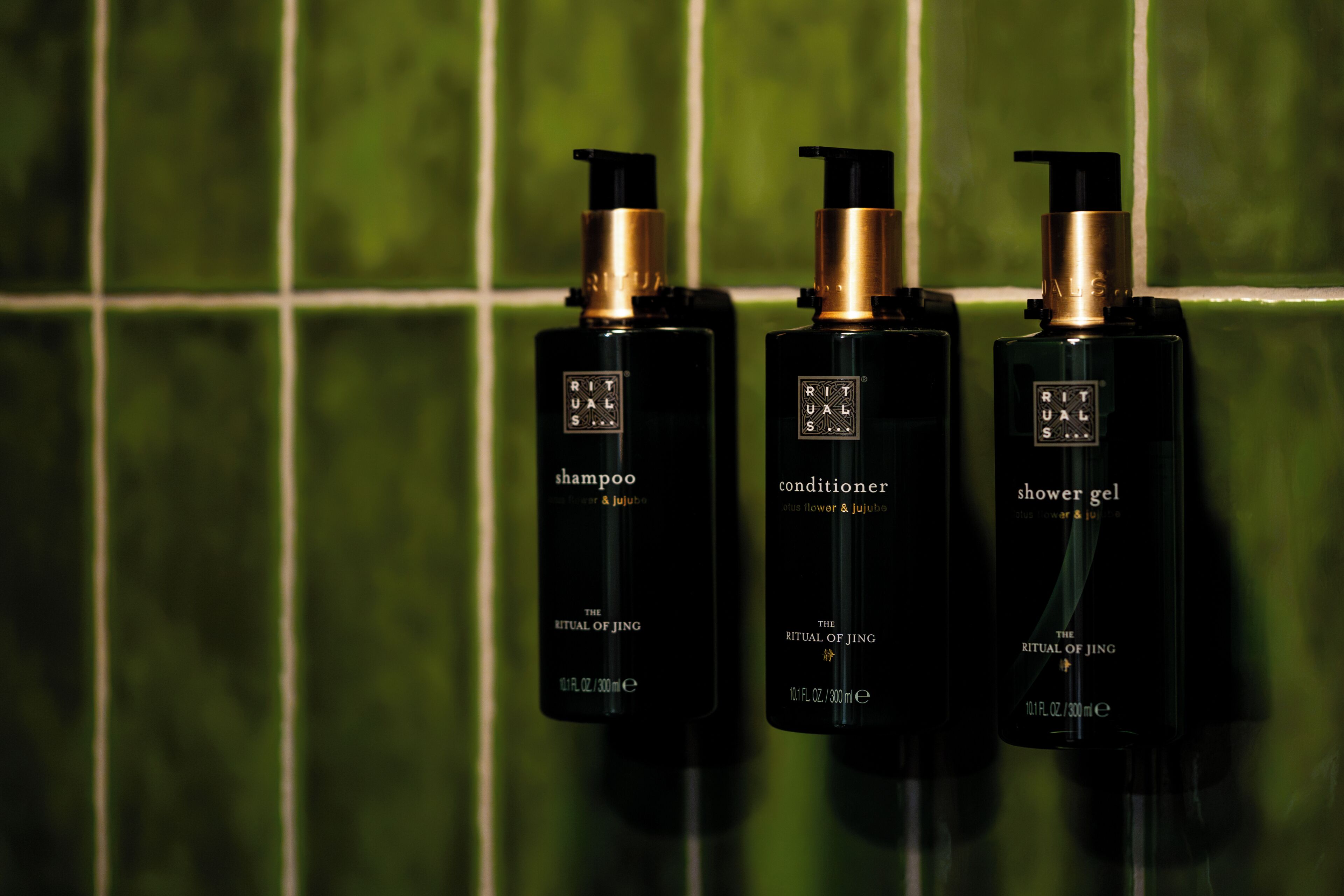 Three bottles of Rituals products against a green tiled wall.