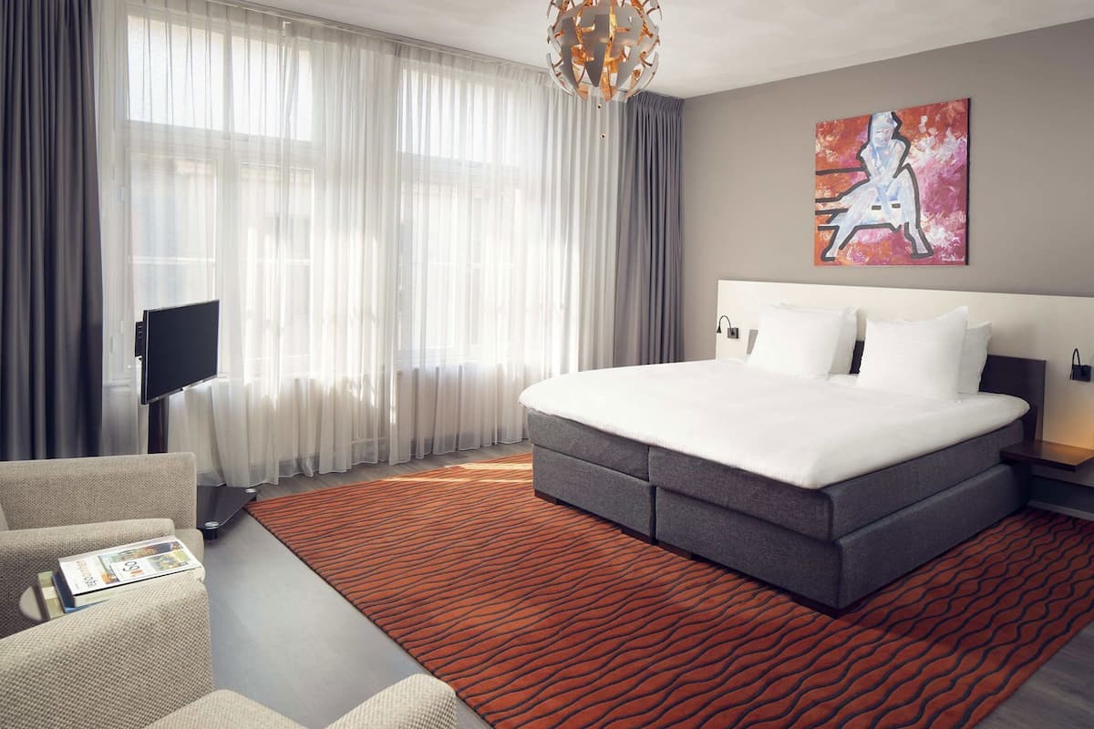 A modern hotel room with a large bed, a flat-screen TV, a sofa, and a painting on the wall.