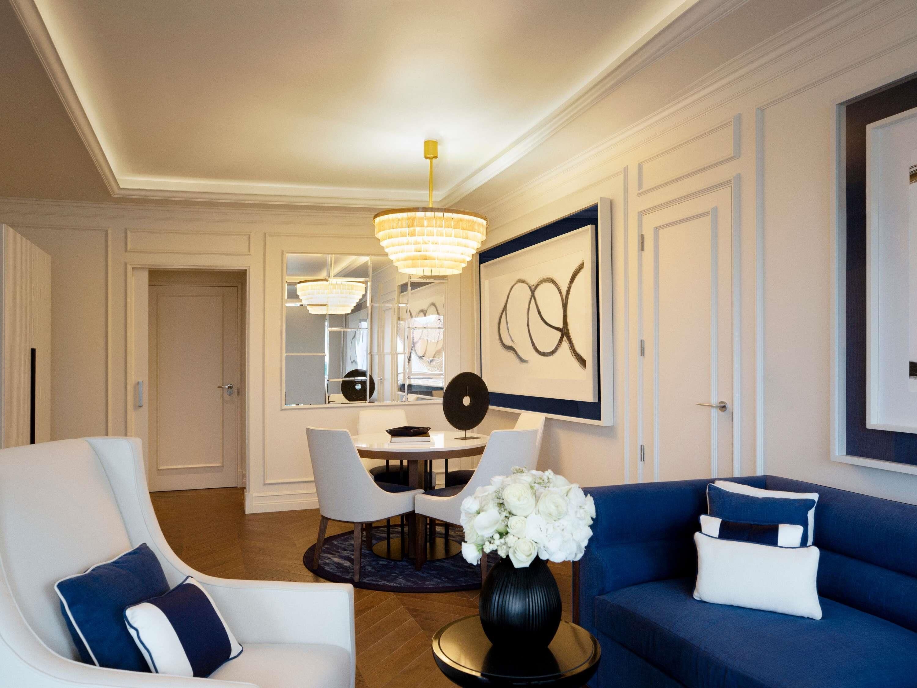 A modern living room with a dining area, a chandelier, and a framed abstract painting.