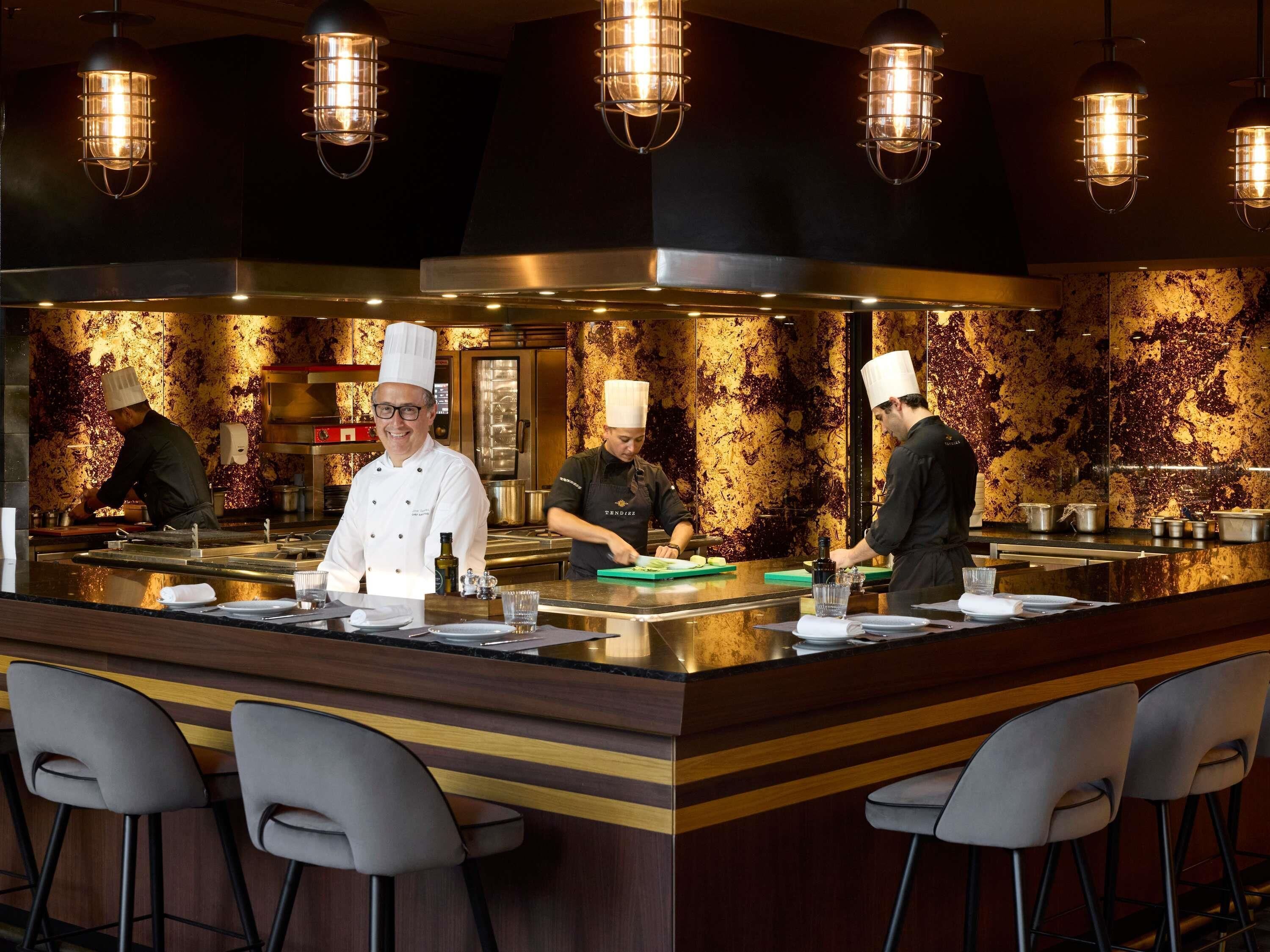 A modern kitchen with chefs at work, a bar area with stools, and a decorative backsplash.
